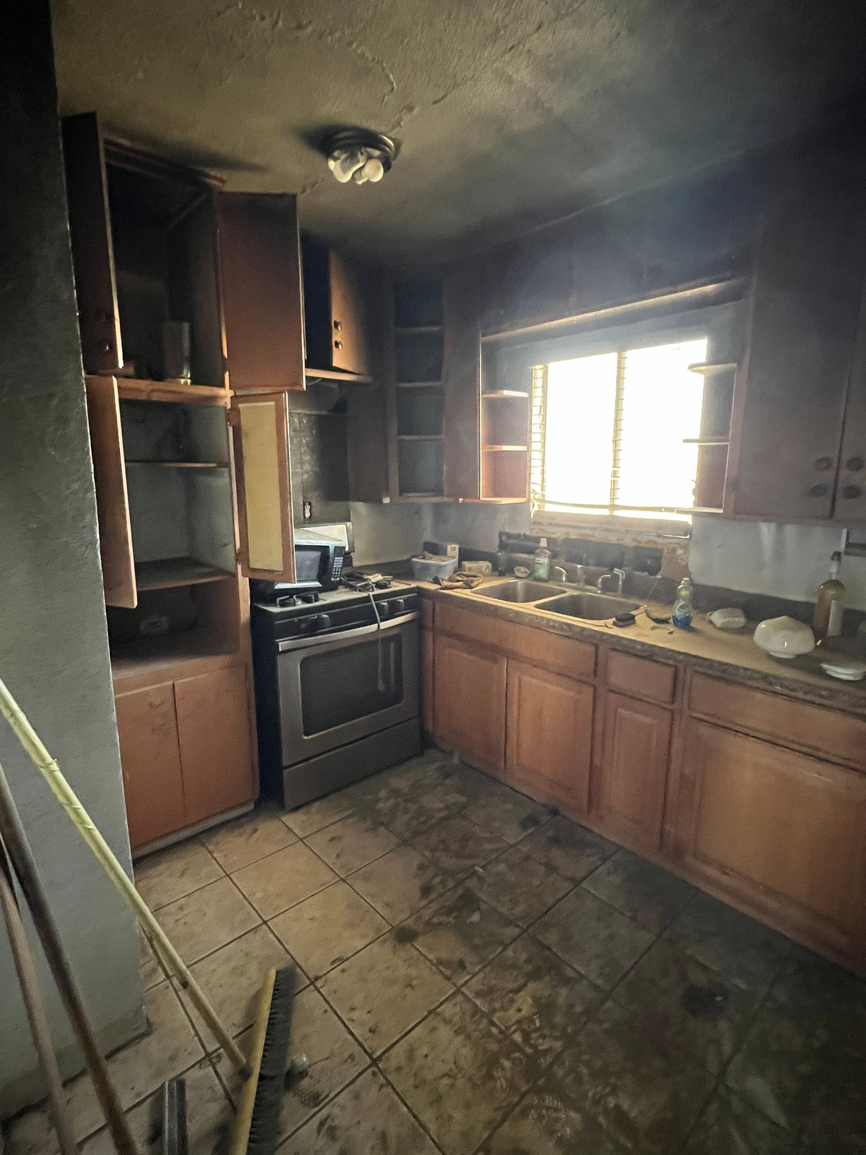 California home with charred siding and smoke staining around a boarded-up window